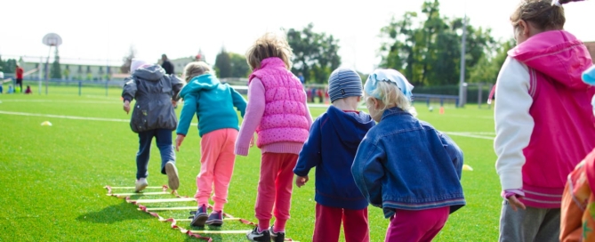 Children playing on a grassy field, climbing wooden ladders and enjoying outdoor activities together.